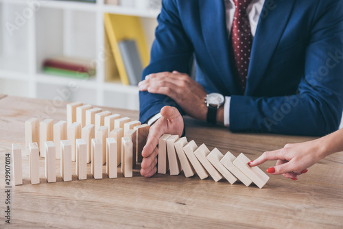 cropped view of woman pushing wooden block and risk manager stopping domino effect photo