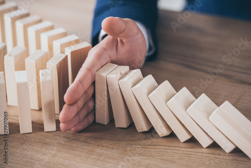partial view of risk manager blocking domino effect of falling wooden blocks photo