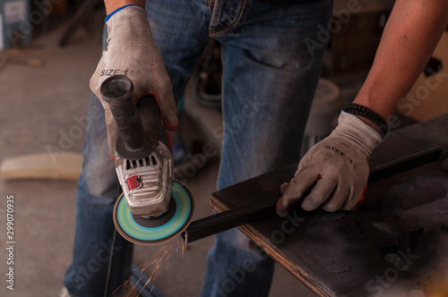 Hands of a craftsman with working gloves cutting an iron bar with the electric grinder