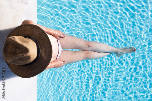 Woman sitting on the steps of a swimming pool with a hat on from overhead