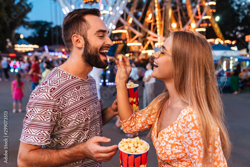 Positive loving couple in amusement park eat popcorn.