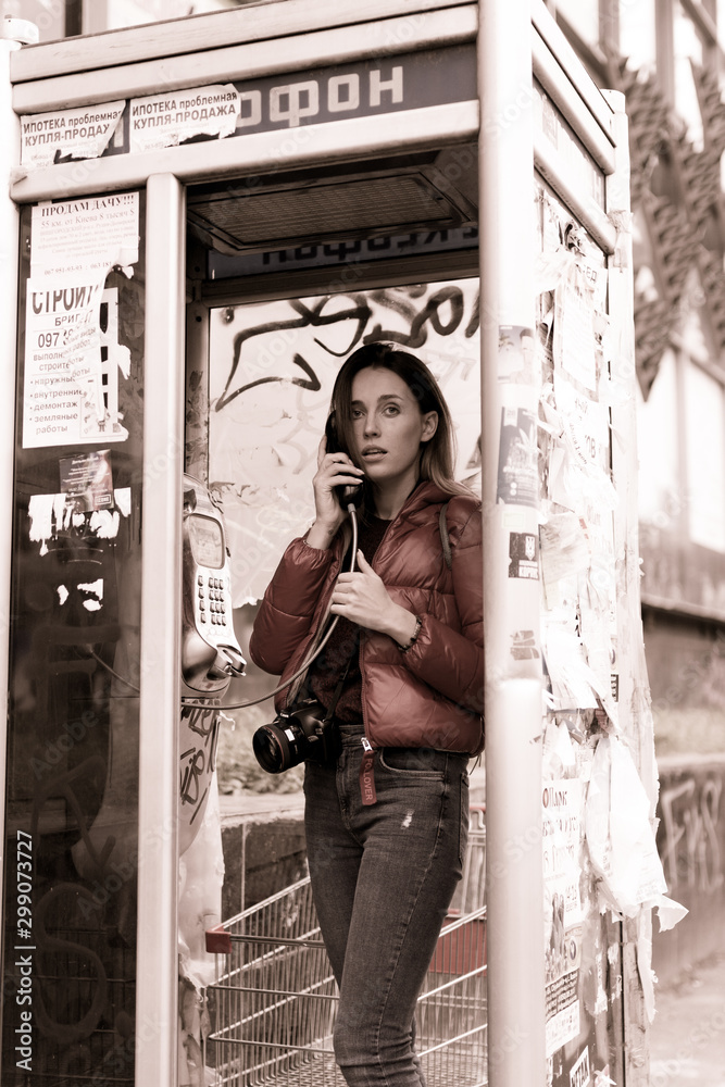 Obraz premium Young woman calling in a phone cabin.