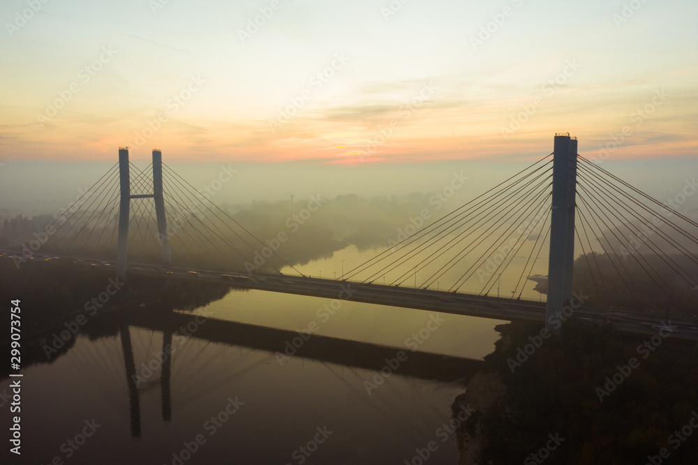 Obraz premium Aerial view of the Siekierkowski Bridge in beautiful fog. Warsaw, Poland. Drone shot at the traffic of vehicle traveling in traffic jam on a bridge over a river.