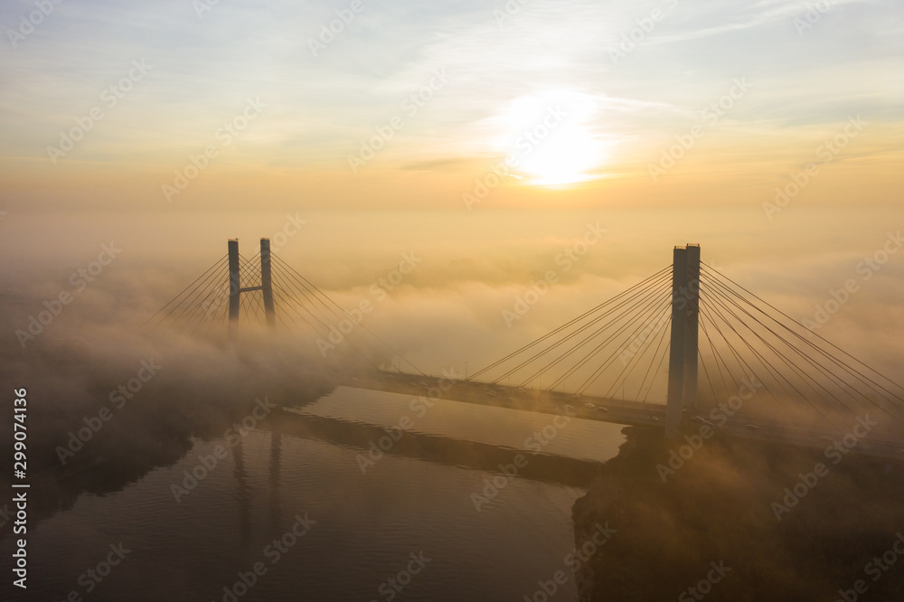 Obraz premium Aerial view of the Siekierkowski Bridge in beautiful fog. Warsaw, Poland. Drone shot at the traffic of vehicle traveling in traffic jam on a bridge over a river.