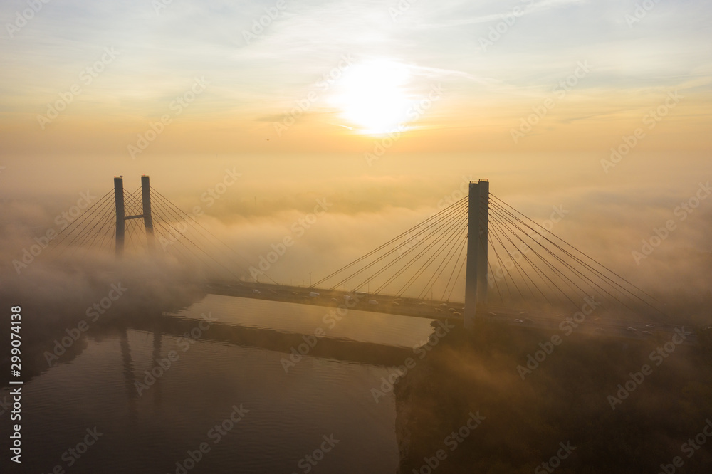 Aerial view of a bridge with cars in the fog. Warsaw. Poland. Drone shot at the traffic of a vehicle traveling in traffic jam on a bridge over a river. Drone shot into the fog at sunrise over a bridg