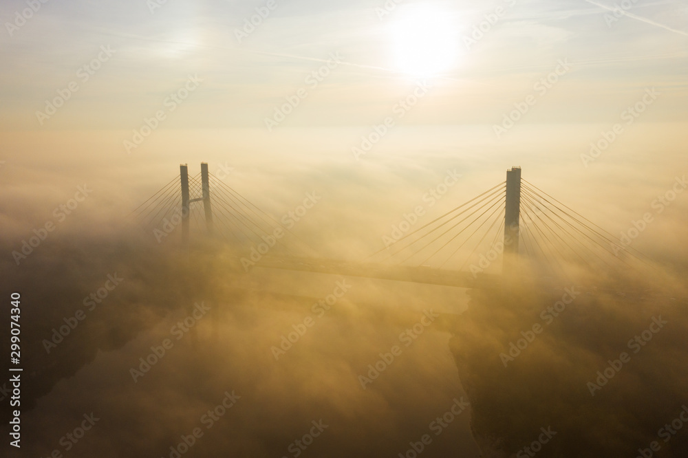 Fototapeta premium Aerial view of morning traffic over a bridge Siekierkowski, with dense fog at sunrise. Warsaw. Poland. Drone flies along a low fog bridge at sunrise.