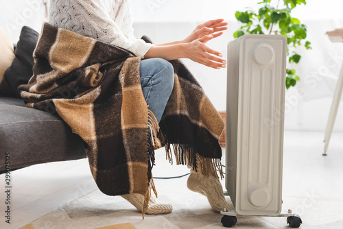 Tableau sur toile cropped view of girl with blanket warming up with heater in cold room