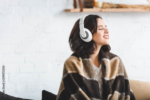 happy woman with closed eyes in blanket listening music with headphones