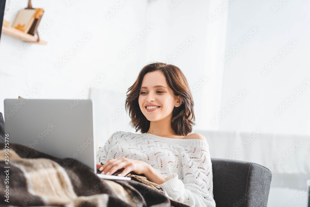 beautiful happy woman in blanket using laptop on sofa in cozy living room beautiful happy woman in blanket using laptop on sofa in cozy living room