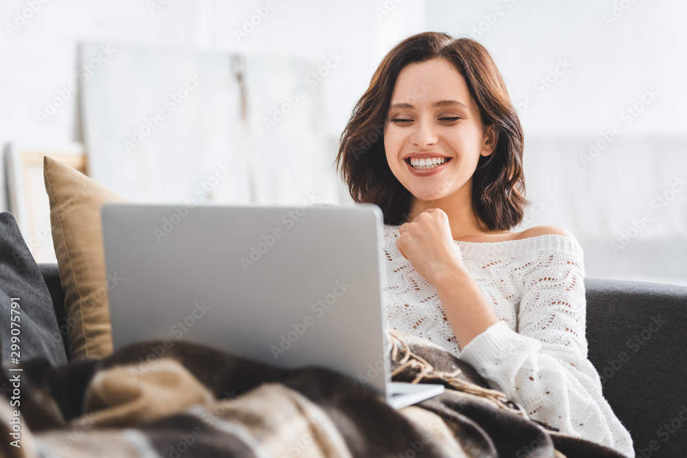 beautiful smiling girl in blanket using laptop on sofa in cozy living room beautiful smiling girl in blanket using laptop on sofa in cozy living room