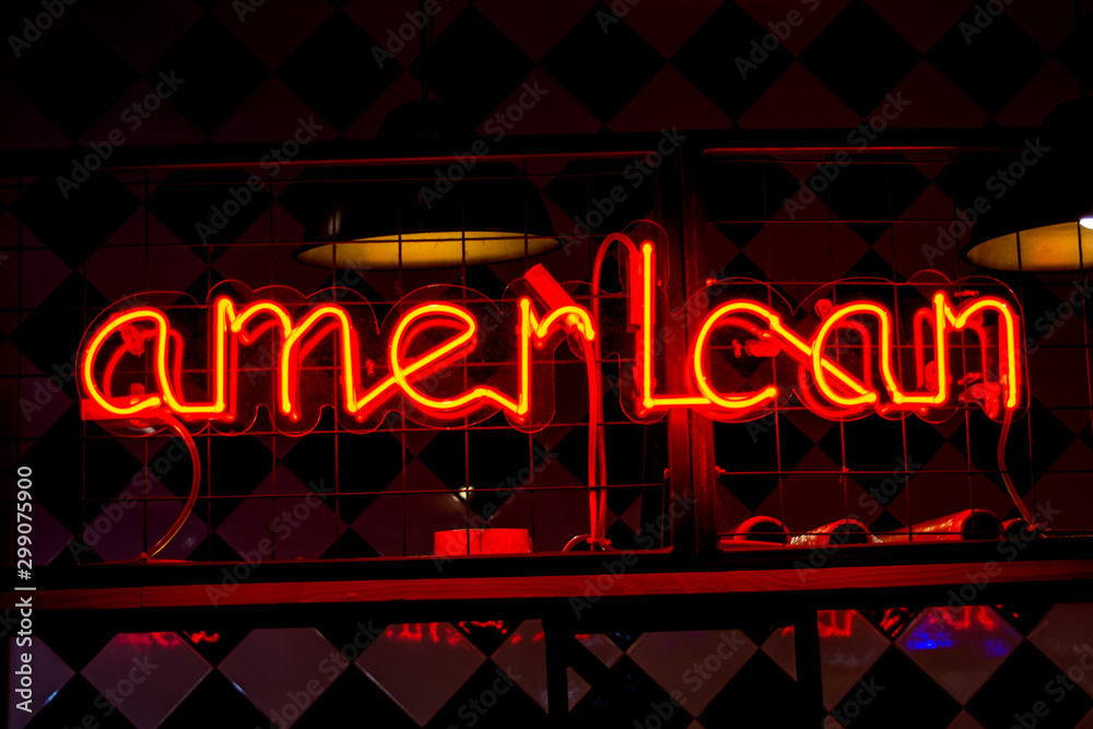 Glowing Neon red sign AMERICAN and blurred lights on black background.