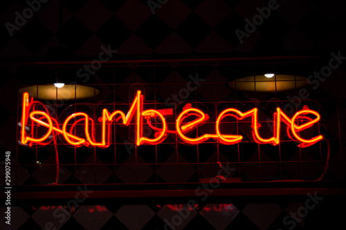 Glowing Neon red sign BARBECUE and blurred lights on black background.