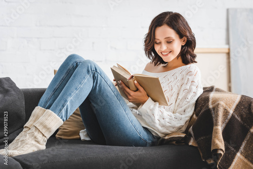 smiling girl reading book on sofa at home photo