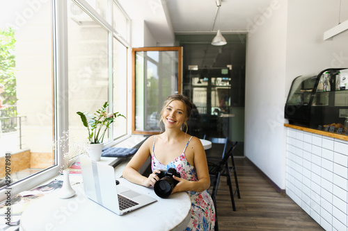 Young female photographer sitting with laptop and camera at cafe. photo