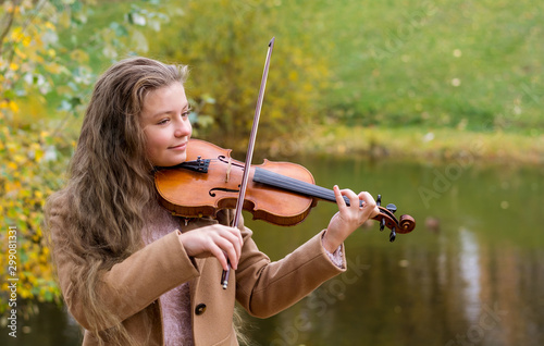 Girl playing the violin and smiling in the autumn park at a lake background.