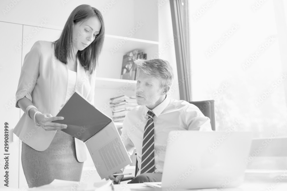 Two business people looking a red file in a small office in a real life business Two business people looking a red file in a small office in a real life business