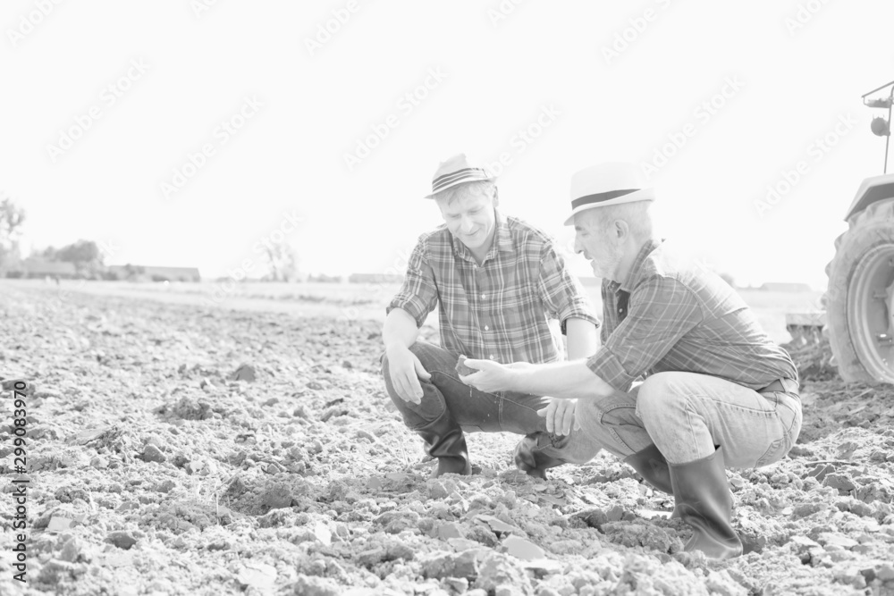 Black and white photo of Mature farmer holding soil while senior farmer discussing in field Black and white photo of Mature farmer holding soil while senior farmer discussing in field