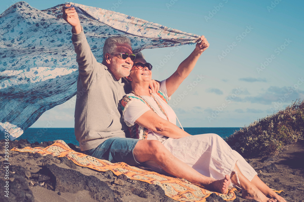 Happy senior caucasian couple enjoy the outdoor leisure activity together - active old people in love have fun under the sun - ocean and nature in background - obrazy, fototapety, plakaty 