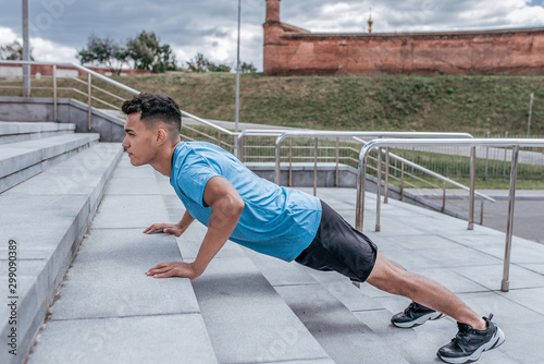 Athletic man, push ups from concrete steps, summer afternoon training in the city, active lifestyle, modern fitness workout, sportswear t-shirt shorts sneakers.