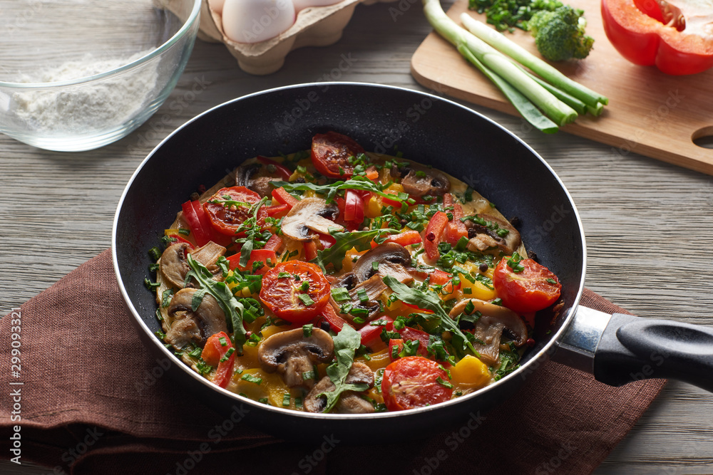 delicious omelet in frying pan with ingredients on table