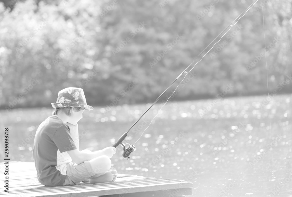 Young boy fishing in lake while sitting on pier