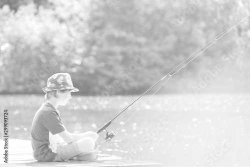 Young boy fishing in lake while sitting on pier