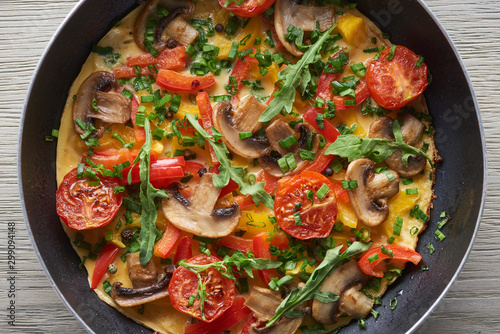 top view of omelet with mushrooms, tomatoes and greens in frying pan
