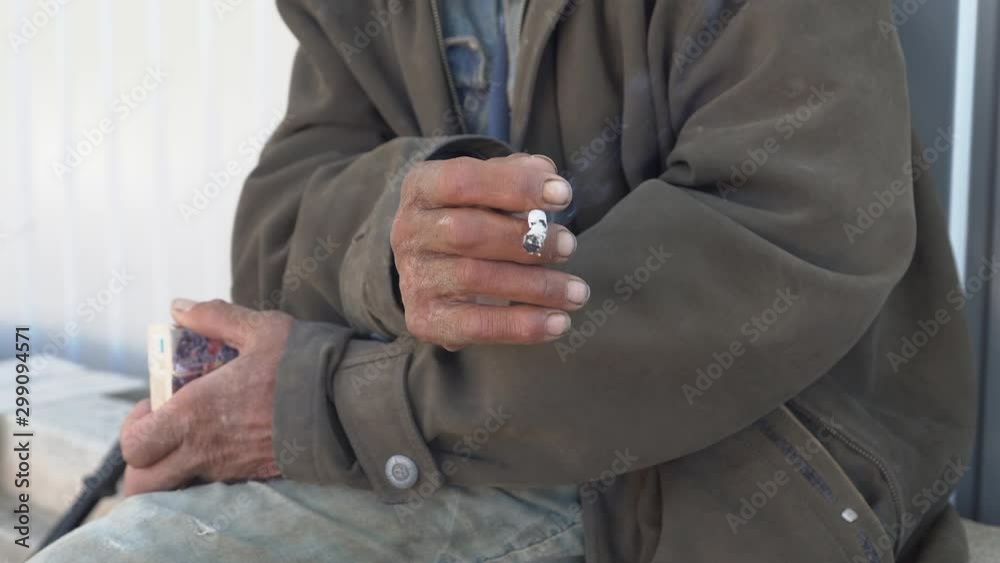 Homeless man smoking outdoors. Close-up of beggar's hand holding a cigarette.