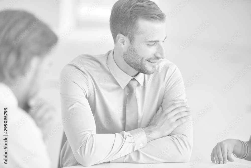 Young businessman smiling while colleagues discussing at table during meeting in office Young businessman smiling while colleagues discussing at table during meeting in office