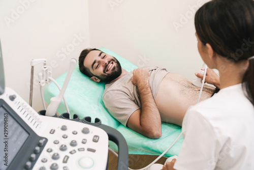Image of smiling man getting abdominal ultrasound scan by female doctor