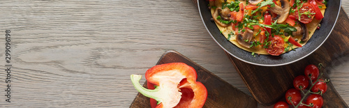 top view of omelet in frying pan on wooden board with bell pepper and tomatoes