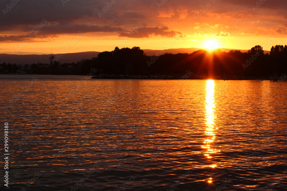 A sunset at a lake is coloring the water with yellow and golden colors. Location: Lake Geneva, Lausanne, Switzerland.