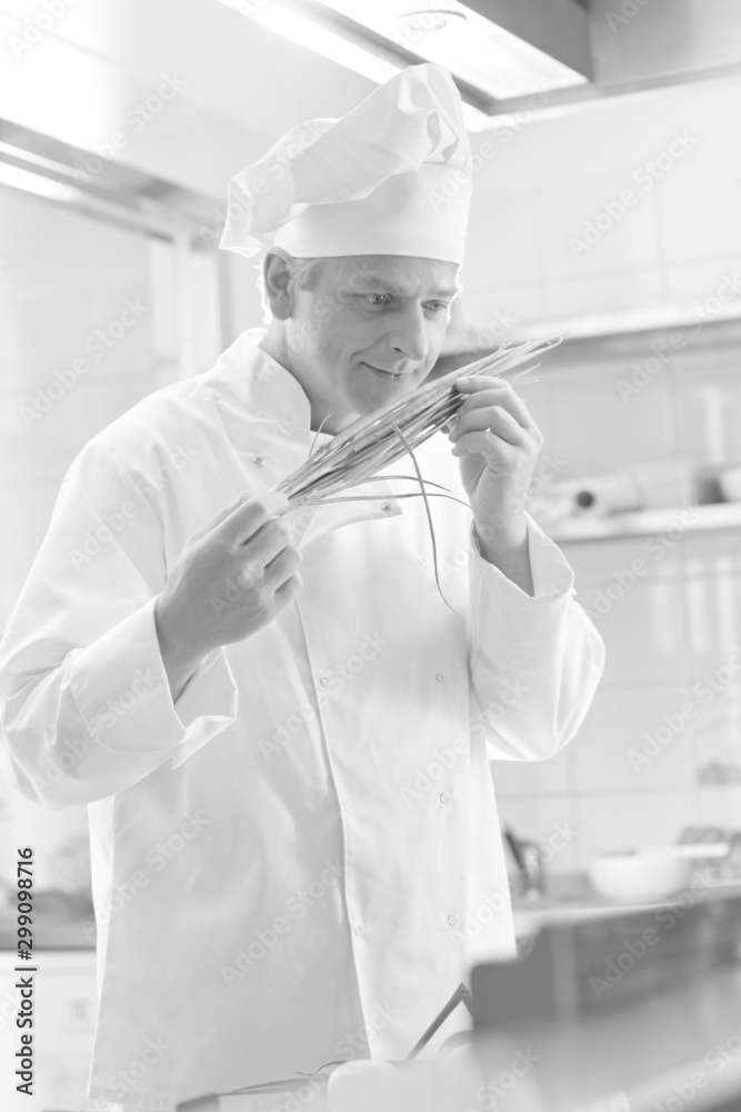 Black and white photo of Confident mature chef smelling onion leaves at kitchen restaurant