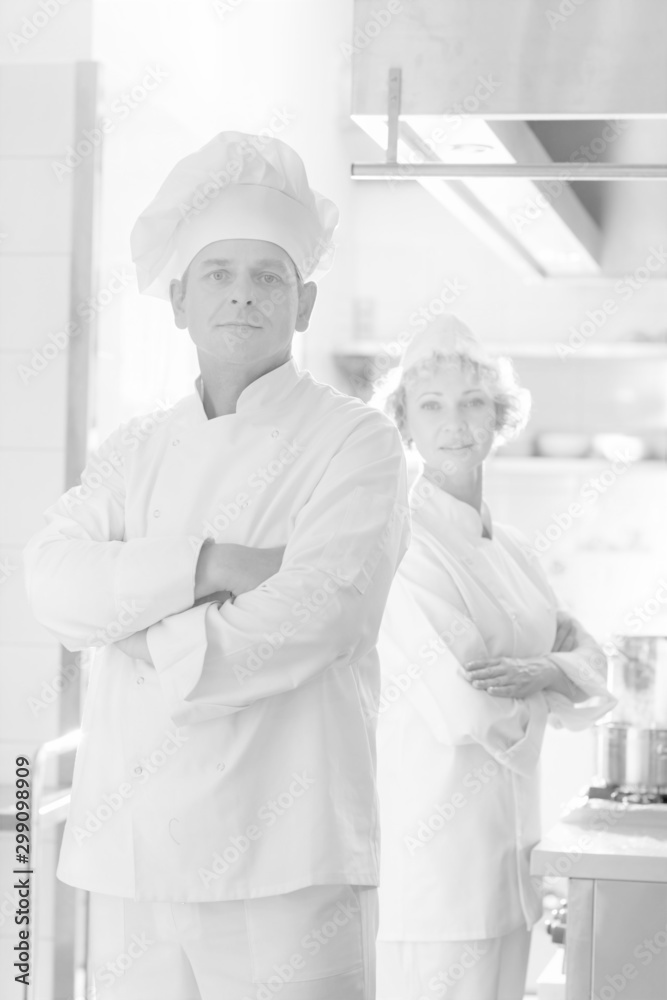 Black and white photo of Confident mature chefs standing with cross arms at kitchen restaurant