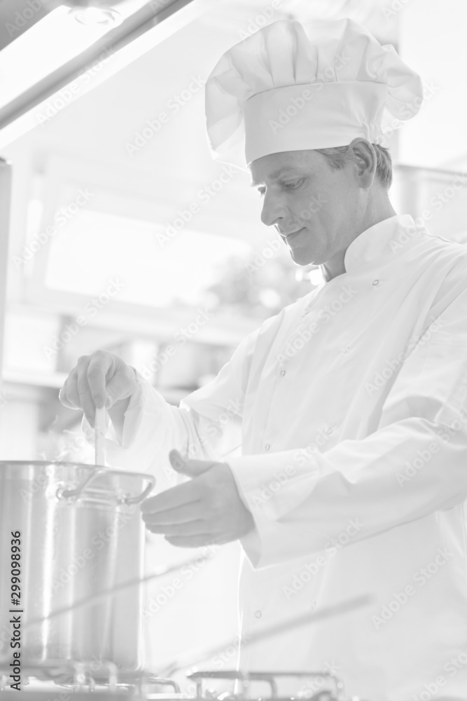 Portrait of mature chef cooking on steel cooking pot in kitchen at restaurant Portrait of mature chef cooking on steel cooking pot in kitchen at restaurant