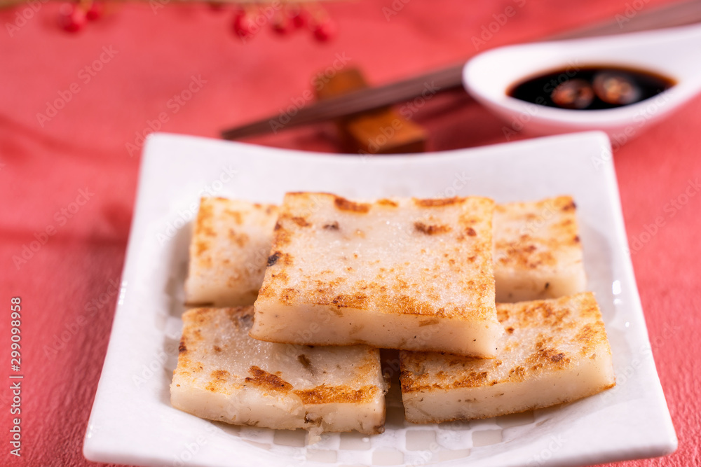 Chinese lunar new year food concept, Delicious turnip radish cake, local cuisine in restaurant with soy sauce on red background, close up, copy space Chinese lunar new year food concept, Delicious turnip radish cake, local cuisine in restaurant with soy sauce on red background, close up, copy space