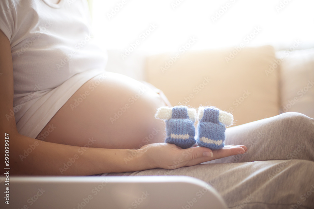 Pregnancy. Happy pregnant woman lying in bed with small blue booties for infant boy at home Pregnancy. Happy pregnant woman lying in bed with small blue booties for infant boy at home