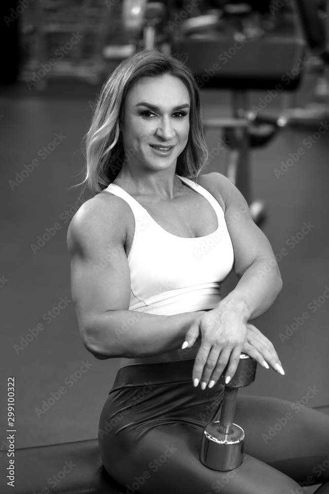 Blonde bodybuilder woman is sitting with dumbbell in the gym and posing BW Blonde bodybuilder woman is sitting with dumbbell in the gym and posing BW