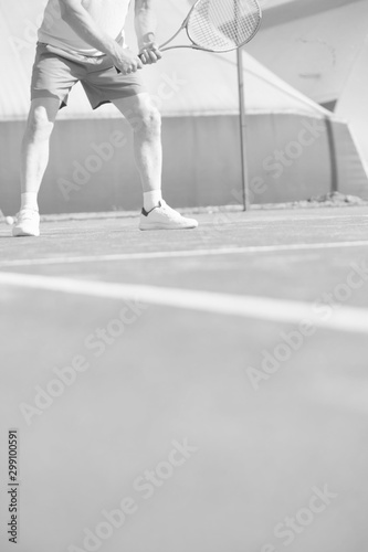 Confident mature man hitting tennis ball with racket on red court
