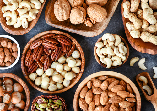 A variety of nuts in wooden bowls from top view. Walnuts, cashew, almond, pistachio, pecan, hazelnut, macadamia nut.