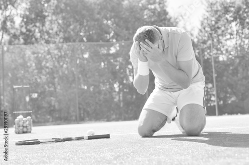 Canvas-taulu Disappointed mature man with head in hands while kneeling by tennis racket on re