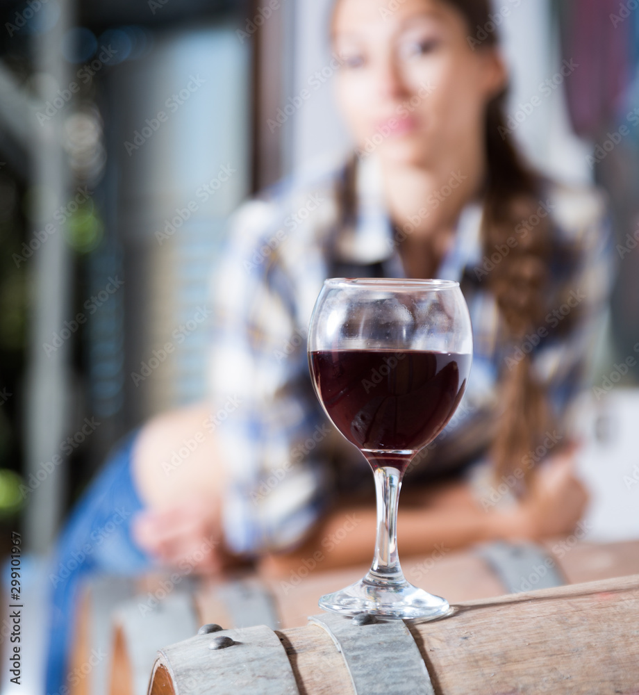 girl looking at glass of red wine standing on wooden barrel in winery girl looking at glass of red wine standing on wooden barrel in winery