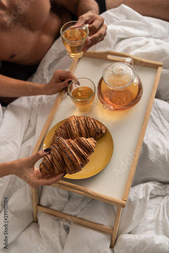 cropped view of couple having tea and croissants for breakfast in bed in the morning