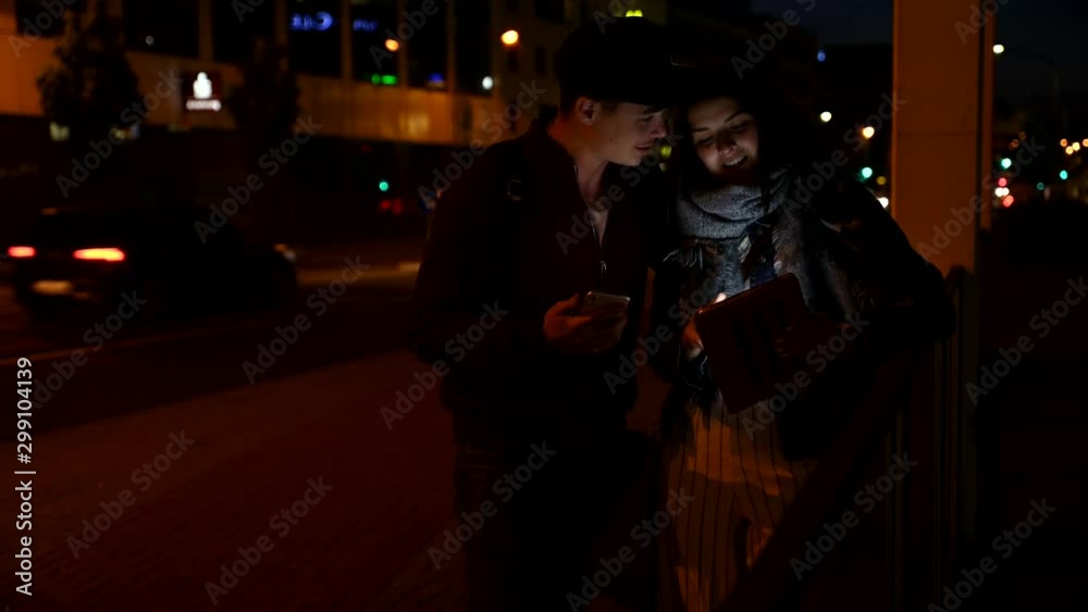 Couple using tablet and smartphone on the street at night Couple using tablet and smartphone on the street at night