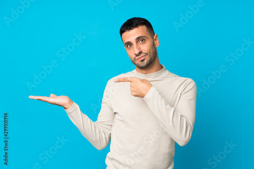 Young man over isolated blue background holding copyspace imaginary on the palm to insert an ad