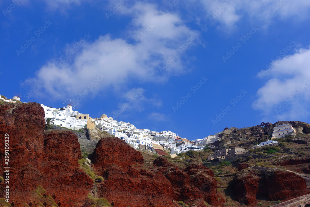 Picturesque village of Oia built on top of a steep cliff as seen from Ammoudi bay in deep blue sky, Santorini island, Cyclades, Greece
