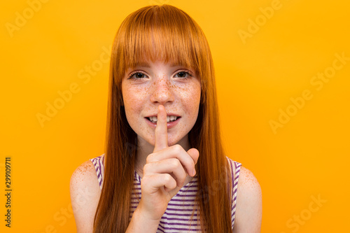 red-haired beautiful girl holds a finger near lips, concept of silence