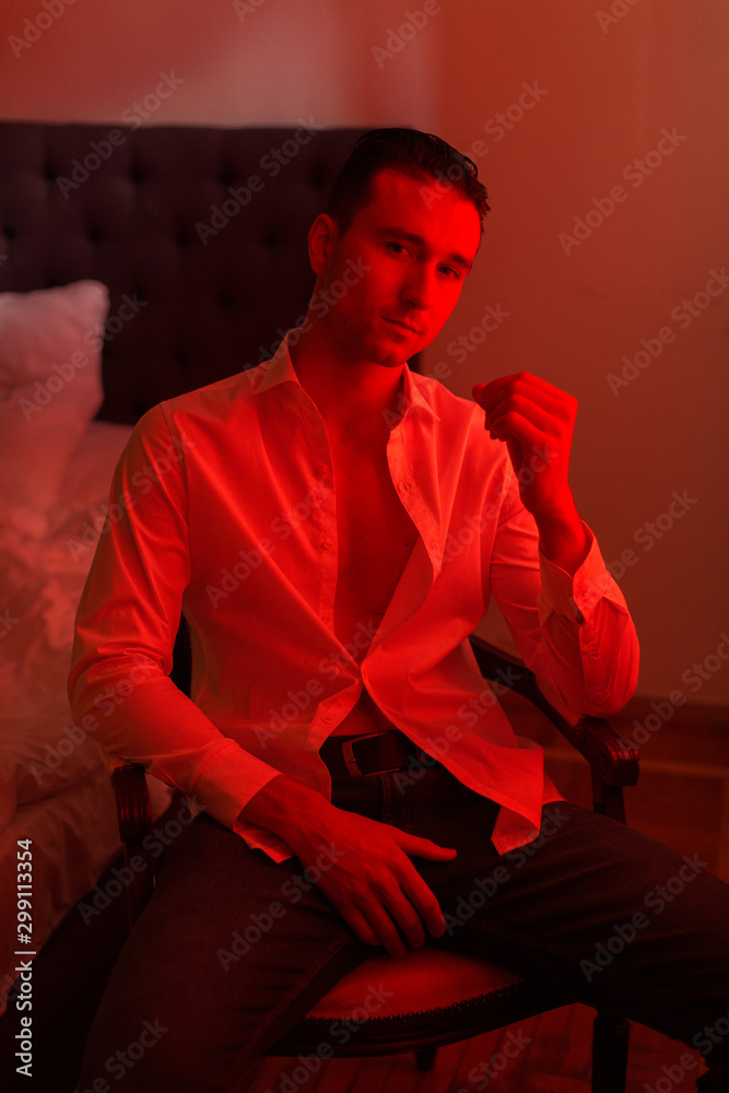 A Young Handsome Man Is Sitting In A Dark Room. Light With A Red Filter.