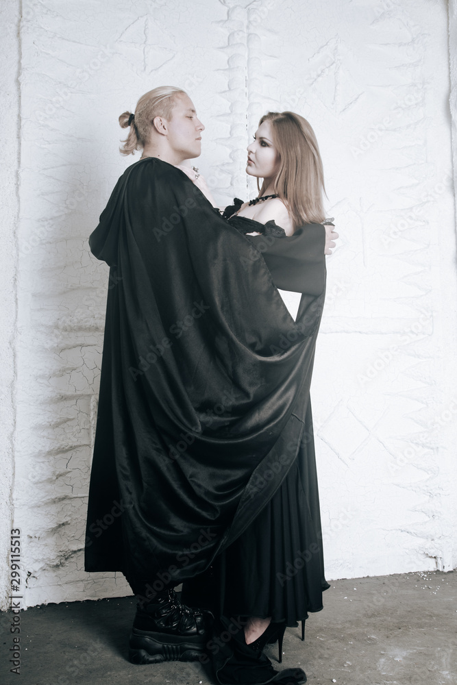 young vampire love couple in black halloween costumes ready for the party. man and woman bite and enjoy each other on white background.