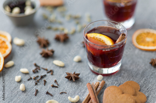 christmas and seasonal drinks concept - hot mulled wine, dry orange slices, raisins with cashew nuts and aromatic spices on grey background